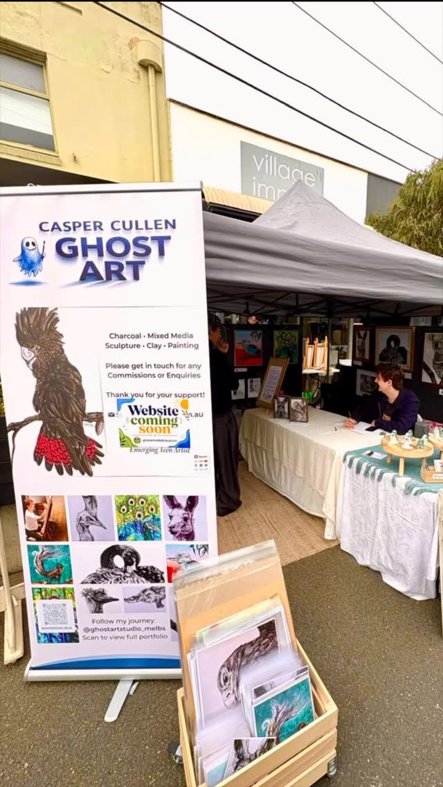 Casper drawing at his Ghost Art market stall, surrounded by his artworks